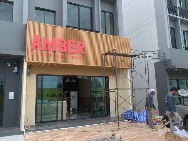 ป้ายตัวอักษร AMBER Bites and Sips สีชมพูแดงบนฟาซาดผนังลายไม้หน้าร้านคาเฟ่