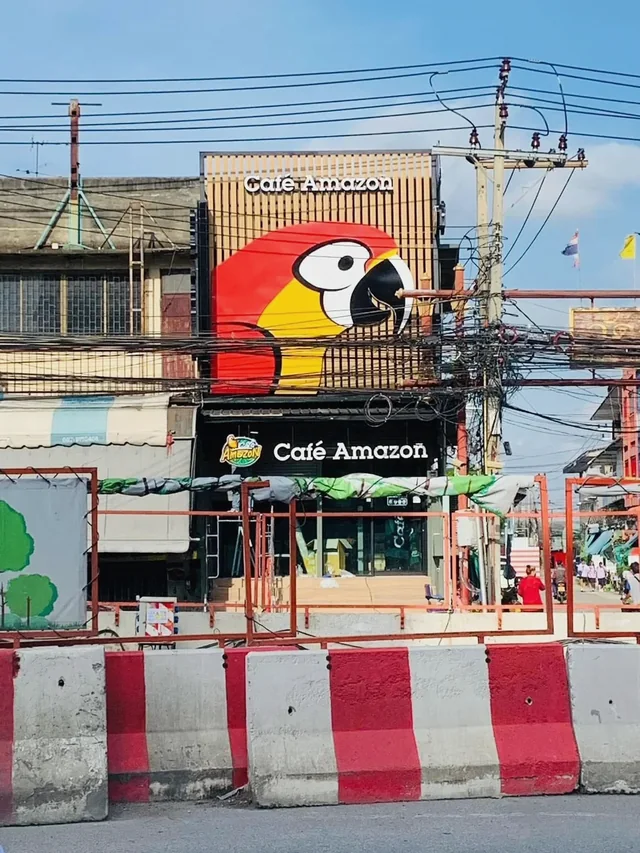 ป้าย Café Amazon พร้อมภาพนกแก้วขนาดใหญ่บนฟาซาดระแนงหน้าอาคารร้านกาแฟ