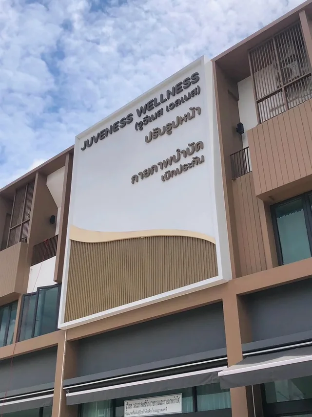 ผลงานป้าย Juveness Wellness Clinic ตัวอักษรโลหะบนฟาซาดสีขาวและแผงตกแต่งลายไม้หน้าอาคาร