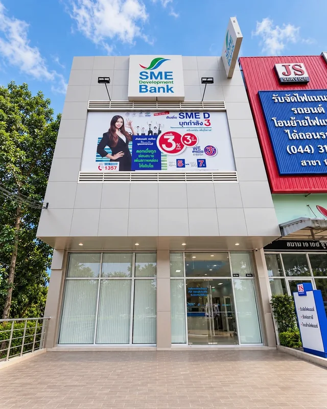 หน้าอาคาร SME Development Bank ฟาซาดแผ่นเรียบสีเทา พร้อมป้ายธนาคารและพื้นที่แบนเนอร์ประชาสัมพันธ์